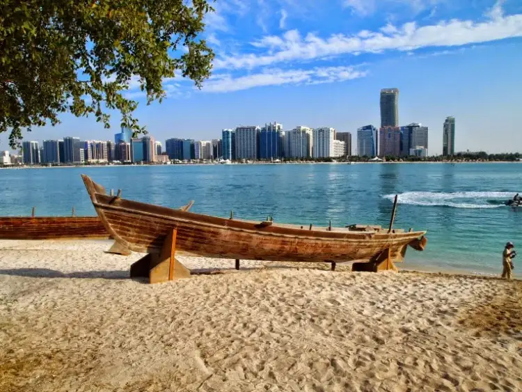 Traditional wooden dhow boat on the Corniche beach with Abu Dhabi skyline