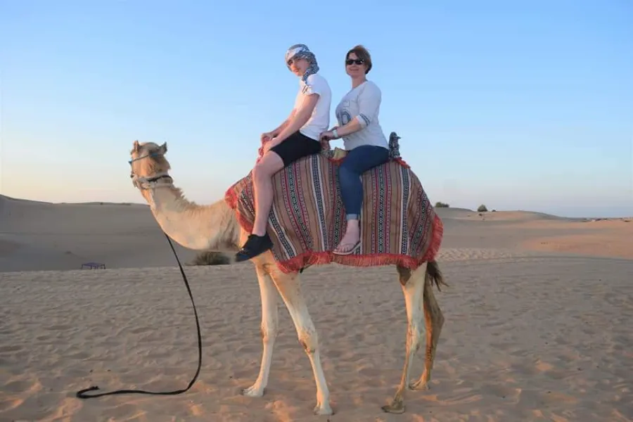 Casual daytime camel ride in the Dubai desert A couple riding a camel together in casual daytime clothing with sandals visible, under a clear blue sky