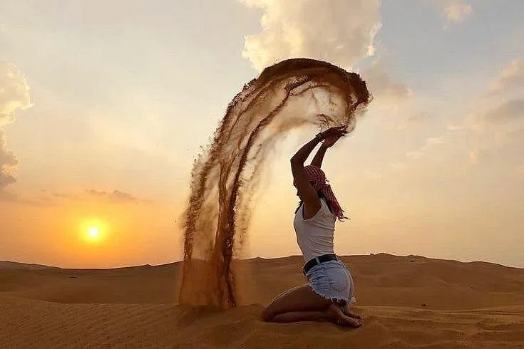 The classic desert safari sand-throw photo A guest kneeling on a dune and throwing a stream of sand into the air at the designated desert safari photo stop