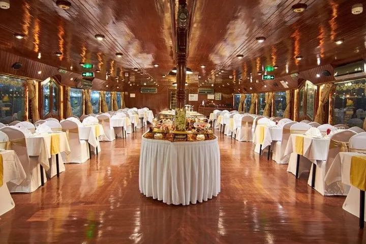 Enclosed dhow dining hall with white-linen tables around a central buffet station