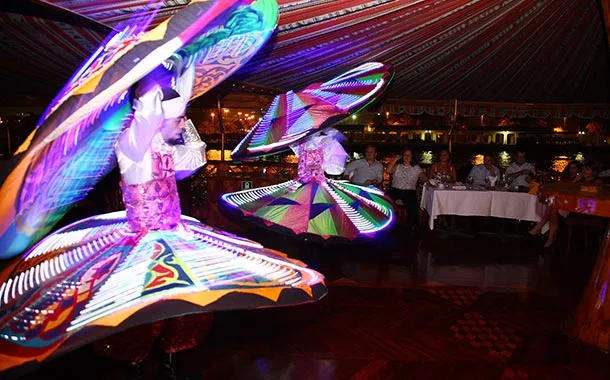 Two performers in illuminated LED tanoura skirts spinning for seated guests on board