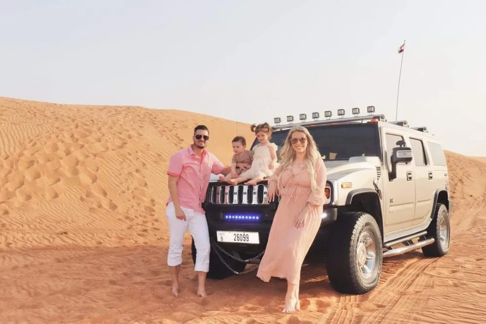 A Hummer desert safari vehicle in Dubai A family posing in front of a white Hummer H2 desert safari vehicle in the dunes