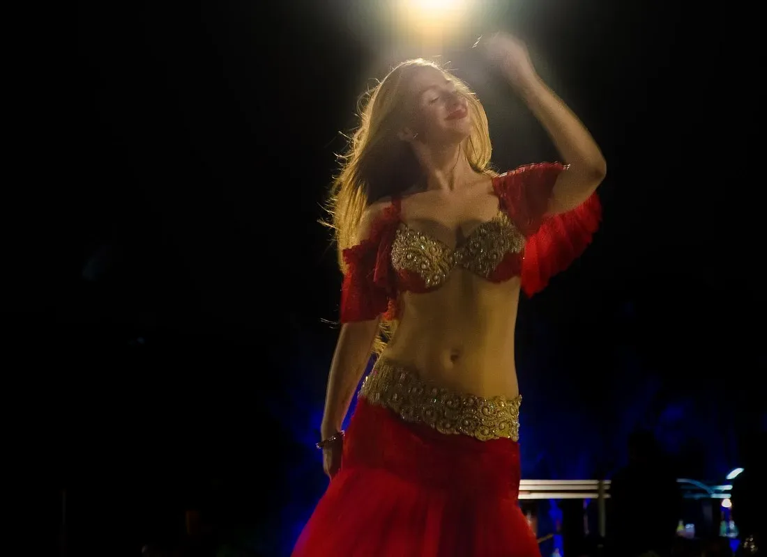 A belly-dance performer in a red and gold costume dancing under stage lights at a Dubai desert safari camp