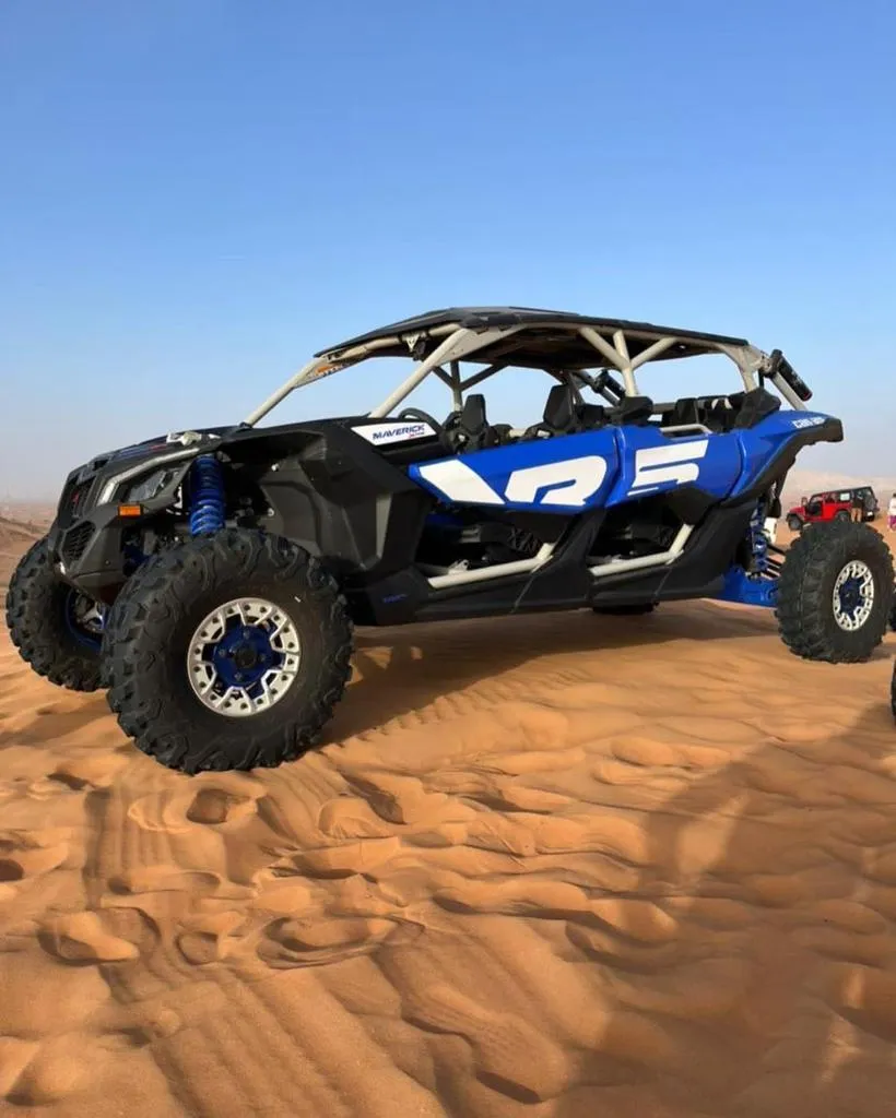 A four-wheel off-road buggy used on a Dubai desert quad-bike tour A black and blue off-road quad buggy with a roll cage parked on sand with city buildings visible in the background