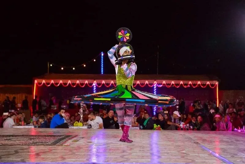 Evening entertainment at a Dubai VIP desert safari camp A tanoura dancer in an illuminated LED skirt performing at night in a decorated Dubai desert safari camp